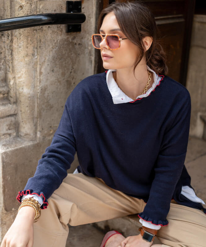 Image of a woman wearing a navy cotton sweater with red ruffle details.