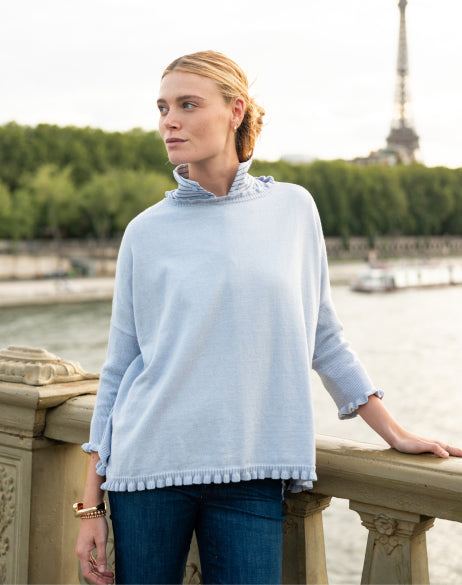 Image of a woman wearing a light blue cotton sweater with ruffle details.