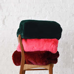 Three Mersea Cozy Cabin Faux Fur Throw Blankets in Pine Punch Pink and Wine folded on a chair