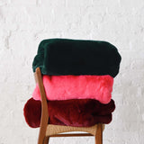 Three Mersea Cozy Cabin Faux Fur Throw Blankets in Pine Punch Pink and Wine folded on a chair