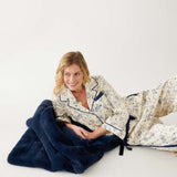 Woman wearing Satin Sailors Lucky Charm  Pajamas laying on folded Mersea Cozy Cabin Faux Fur Throw Blanket in Oxford Blue