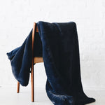 Mersea Cozy Cabin Faux Fur Throw Blanket in Oxford Blue draped over a chair