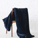 Mersea Cozy Cabin Faux Fur Throw Blanket in Oxford Blue draped over a chair