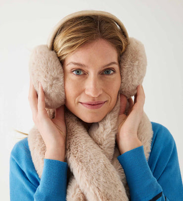 female wearing neutral earmuffs and matching scarf with a striped sweater on a white background