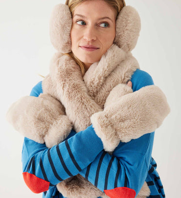 female wearing neutral earmuffs and matching scarf and gloves a striped sweater on white background