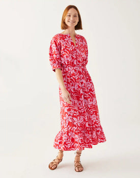 Female wearing a long pink floral dress with sandals in front of white wall