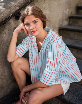 female wearing blue button up top with red stripes sitting on stairs outside 