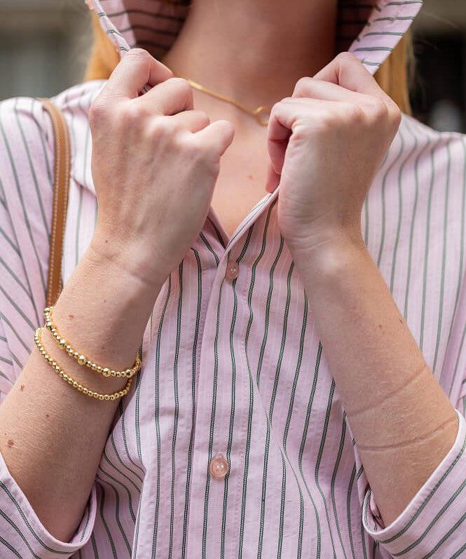 Close up image of a pink striped top with a pop-up collar.