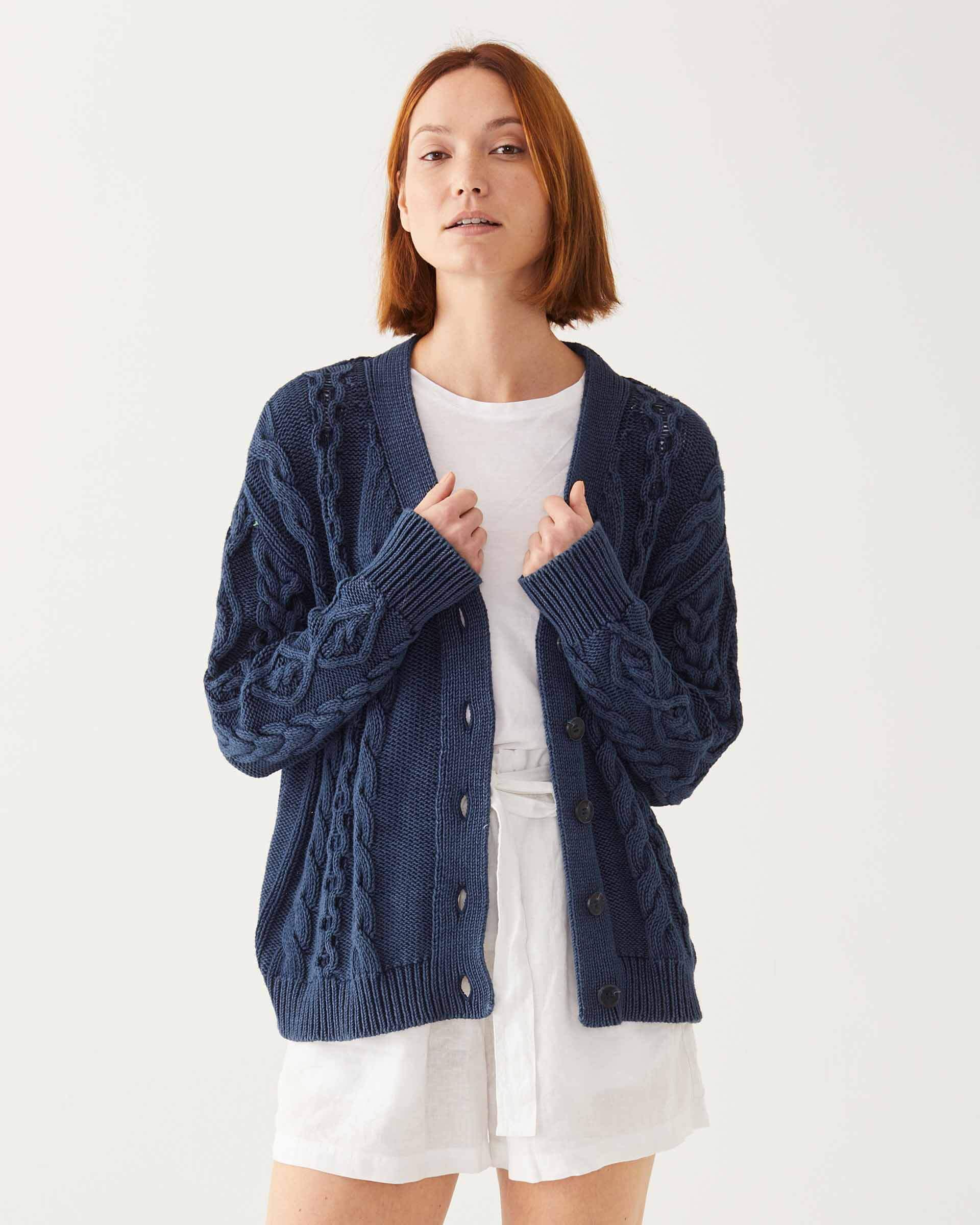 Female wearing a navy blue knitted cardigan in front of white wall