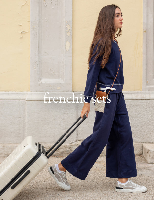 Woman in navy outfit pulling a suitcase with 'frenchi sets' branding.