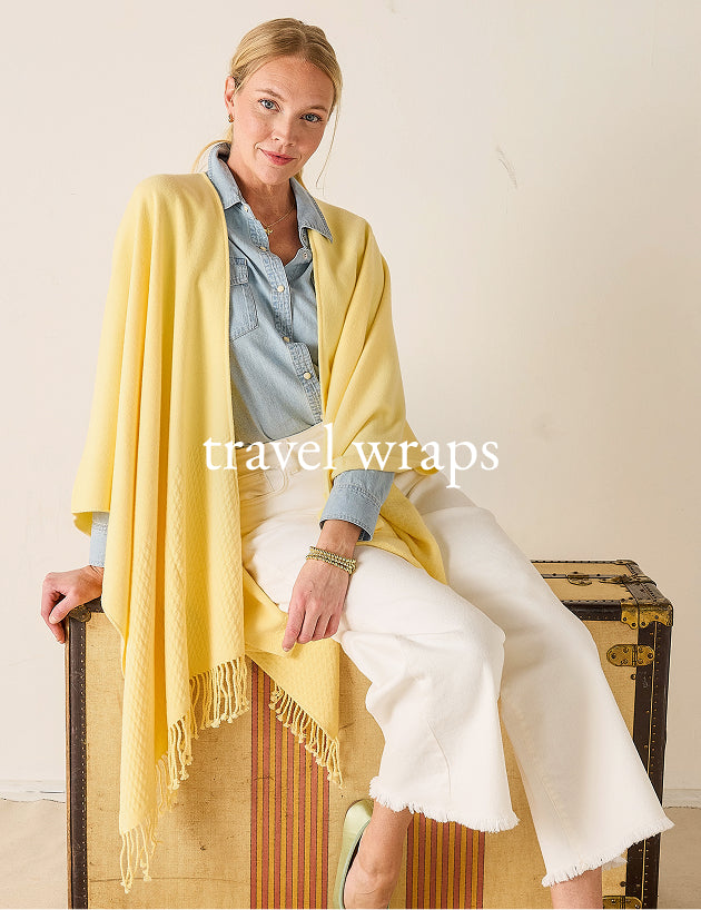 Woman wearing a yellow travel wrap sitting on a wooden bench with a suitcase.