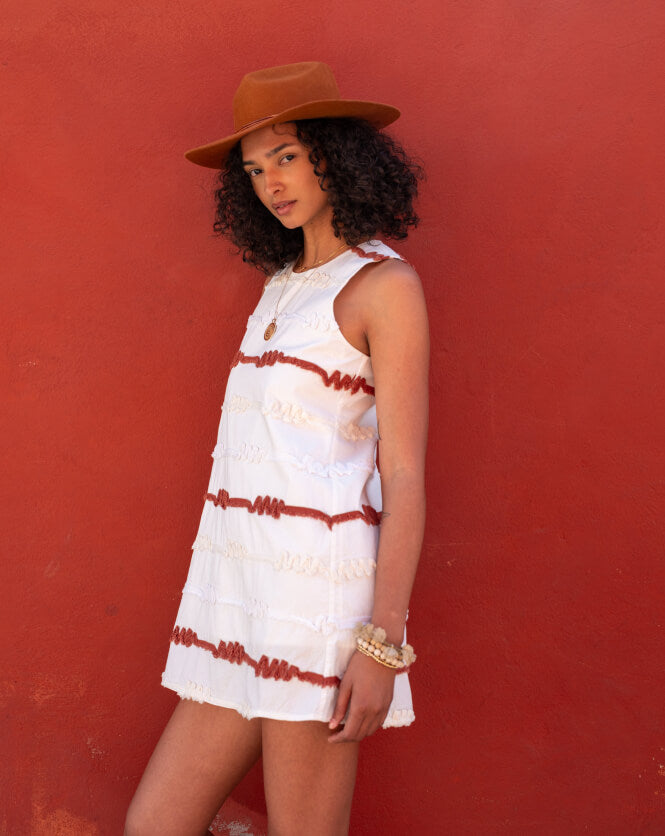 Image of a woman wearing a white sleeveless dress that falls above the knee with orange and white ribbon details