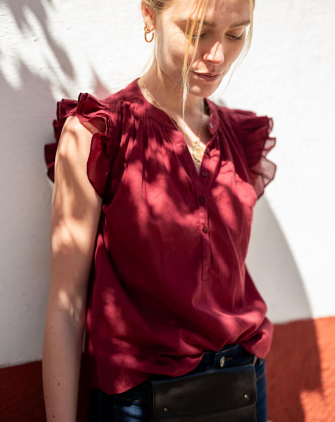 Close up image of a woman wearing a maroon top with ruffle sleeves