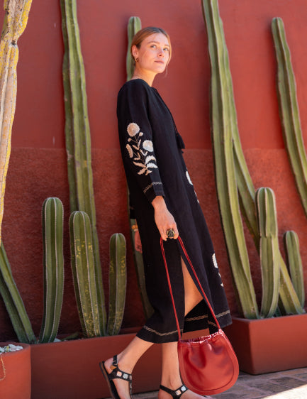 Image of a woman wearing a black linen maxi dress with long sleeves and embroidered details
