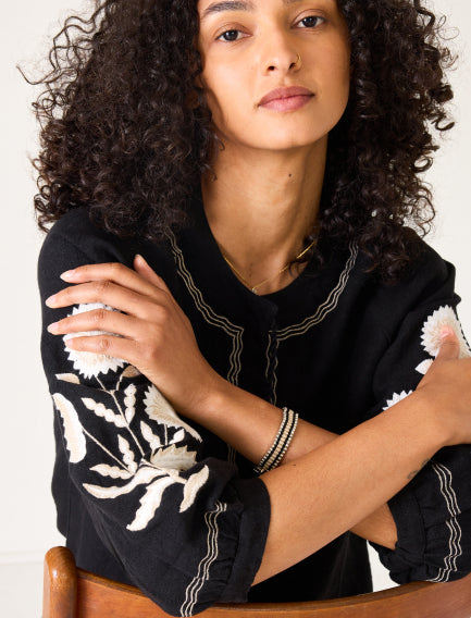 Close up image of a black linen top with long sleeves with embroidered details
