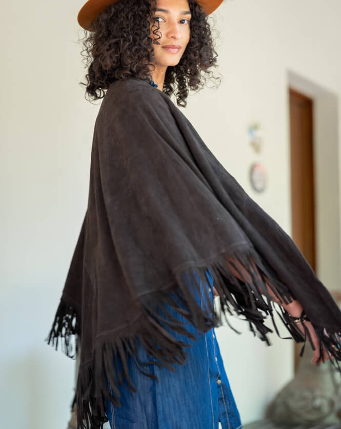 Woman wearing a dark brown fringed shawl over a blue dress indoors.