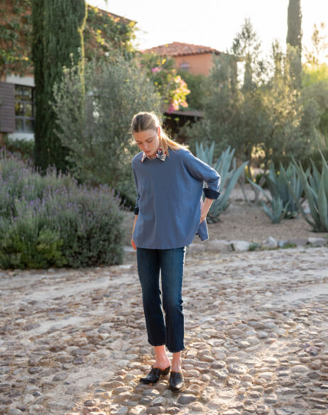 Woman in a blue shirt and jeans walking on a cobblestone path with greenery in the background