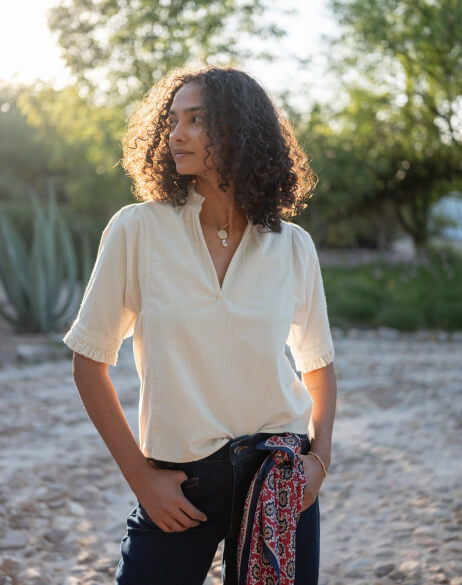 Woman wearing a white blouse with a patterned scarf in a natural setting