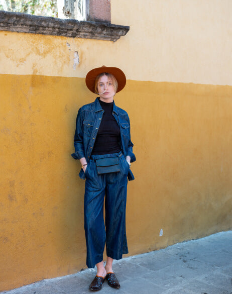 Person wearing a denim outfit and hat against a yellow wall