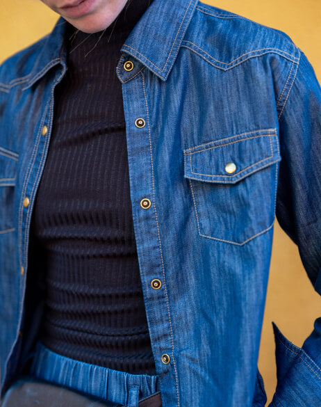 Person wearing a blue denim jacket over a dark sweater against a yellow background
