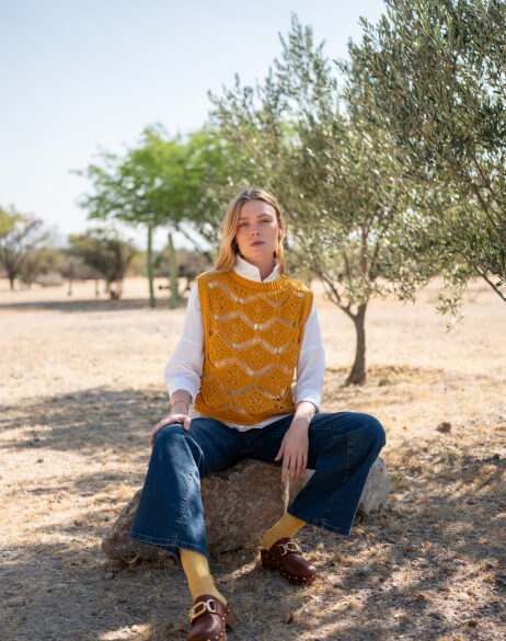 Person sitting outdoors in a natural setting wearing a yellow patterned vest.