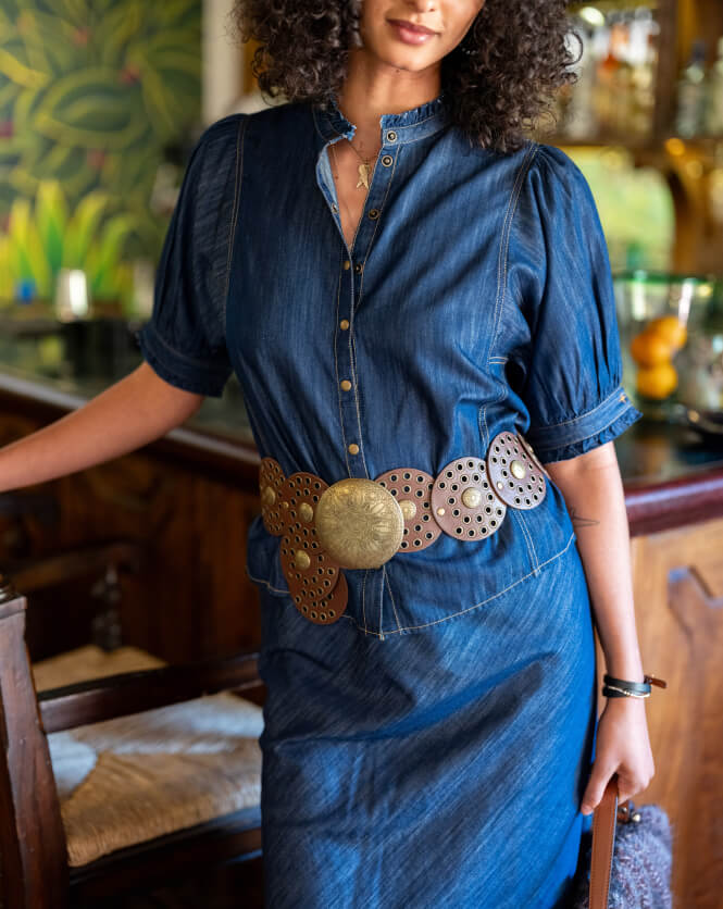 Woman wearing a blue denim dress with a decorative belt in an indoor setting.