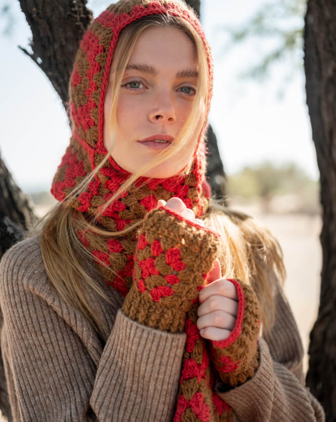 Woman wearing a brown and red crocheted bonnet and gloves outdoors.