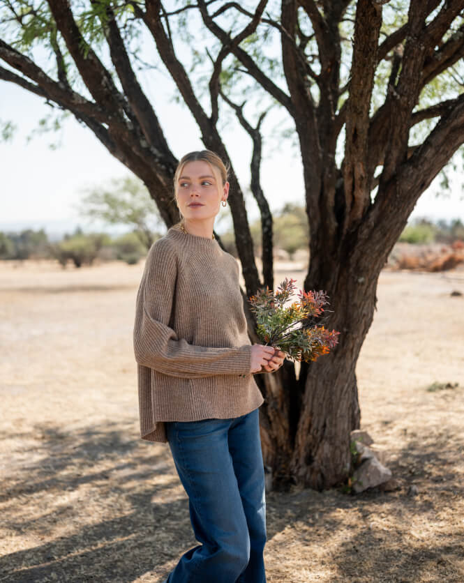 Woman holding flowers standing under a tree in a natural setting
