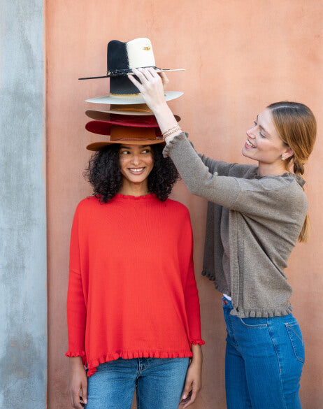 Two women with a stack of hats against a pink wall