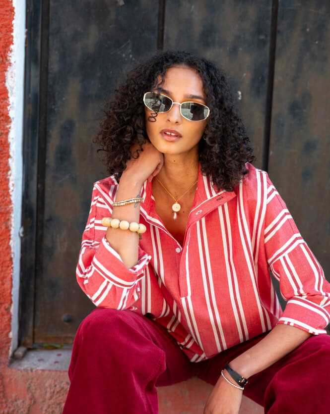 Woman wearing a red and white striped shirt and red pants sitting against a textured wall.