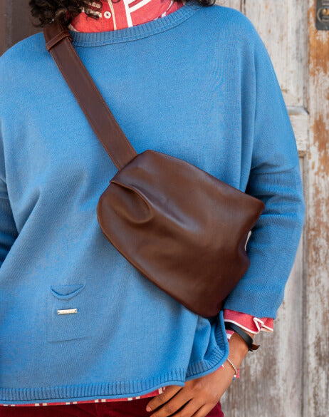 Person wearing a blue sweater with a brown shoulder bag against a wooden background