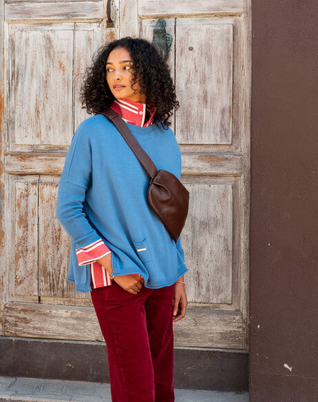 Woman wearing a blue sweater and red pants standing in front of a wooden door.