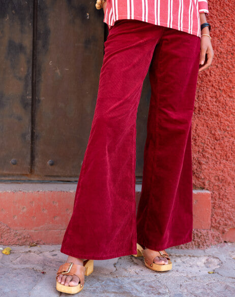 Person wearing red velvet pants standing against a textured wall.