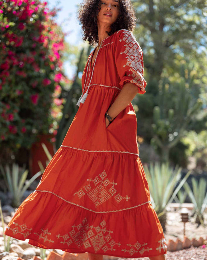Woman wearing an orange dress with white embroidery in a garden setting