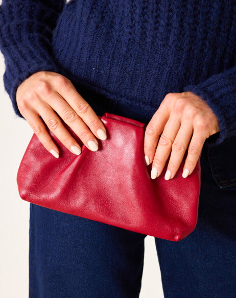 Red clutch held by a person wearing a dark blue sweater and jeans.