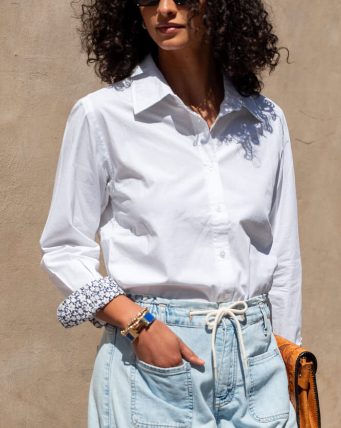 Person wearing a white shirt and light blue jeans against a beige wall.