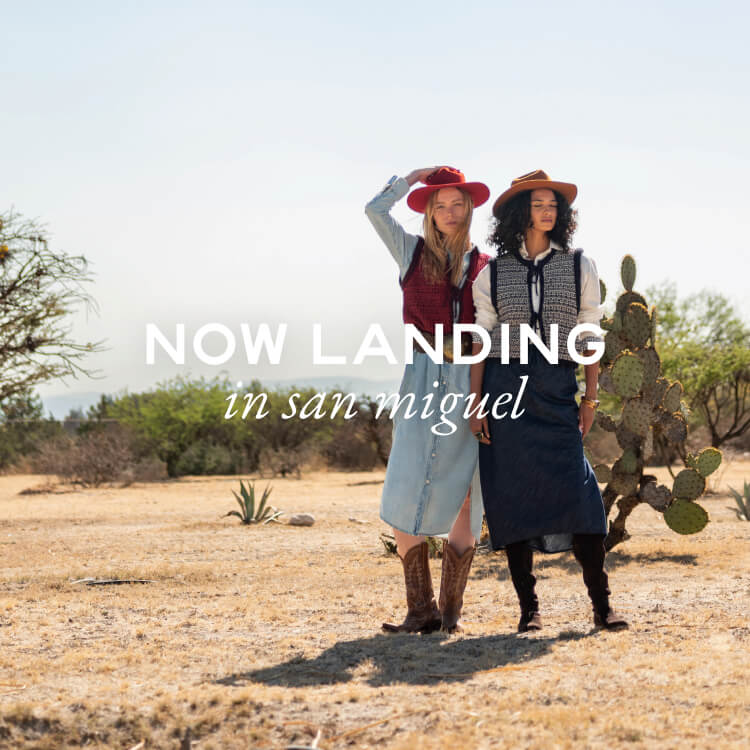 Two women standing in a desert landscape with text 'NOW LANDING in san miguel'.