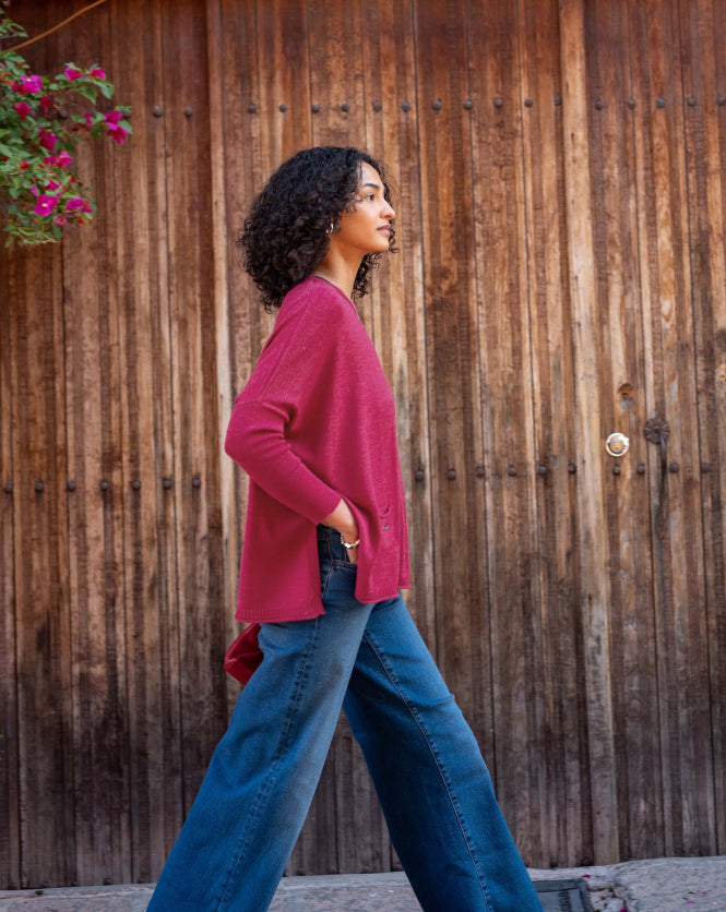 Woman in a pink sweater and blue jeans walking past a wooden door with a plant.