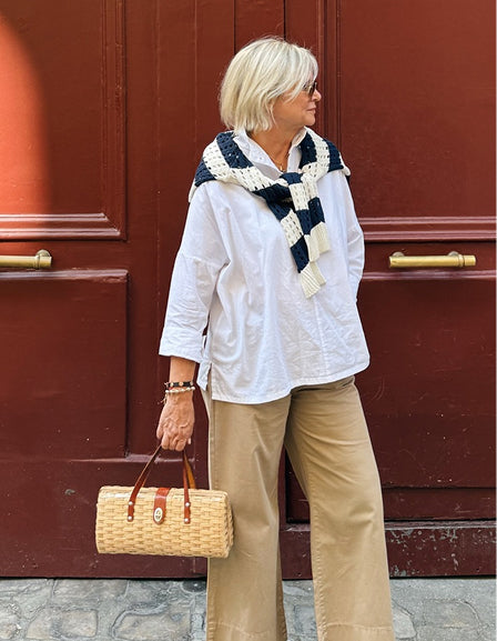 MERSEA women's travel-friendly white oversized button-down shirt paired with a navy and cream knit wrap and straw tote bag.