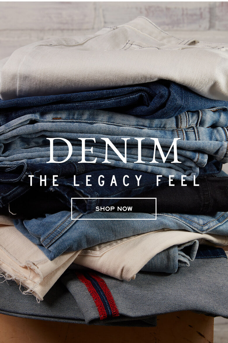 Pile of various denim jeans and neutral-toned clothing. Text: DENIM THE LEGACY FEEL SHOP NOW