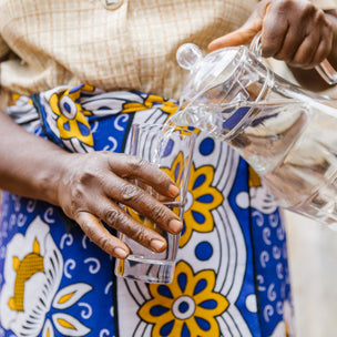 Female pouring water in a glass wearing a blue and yellow dress