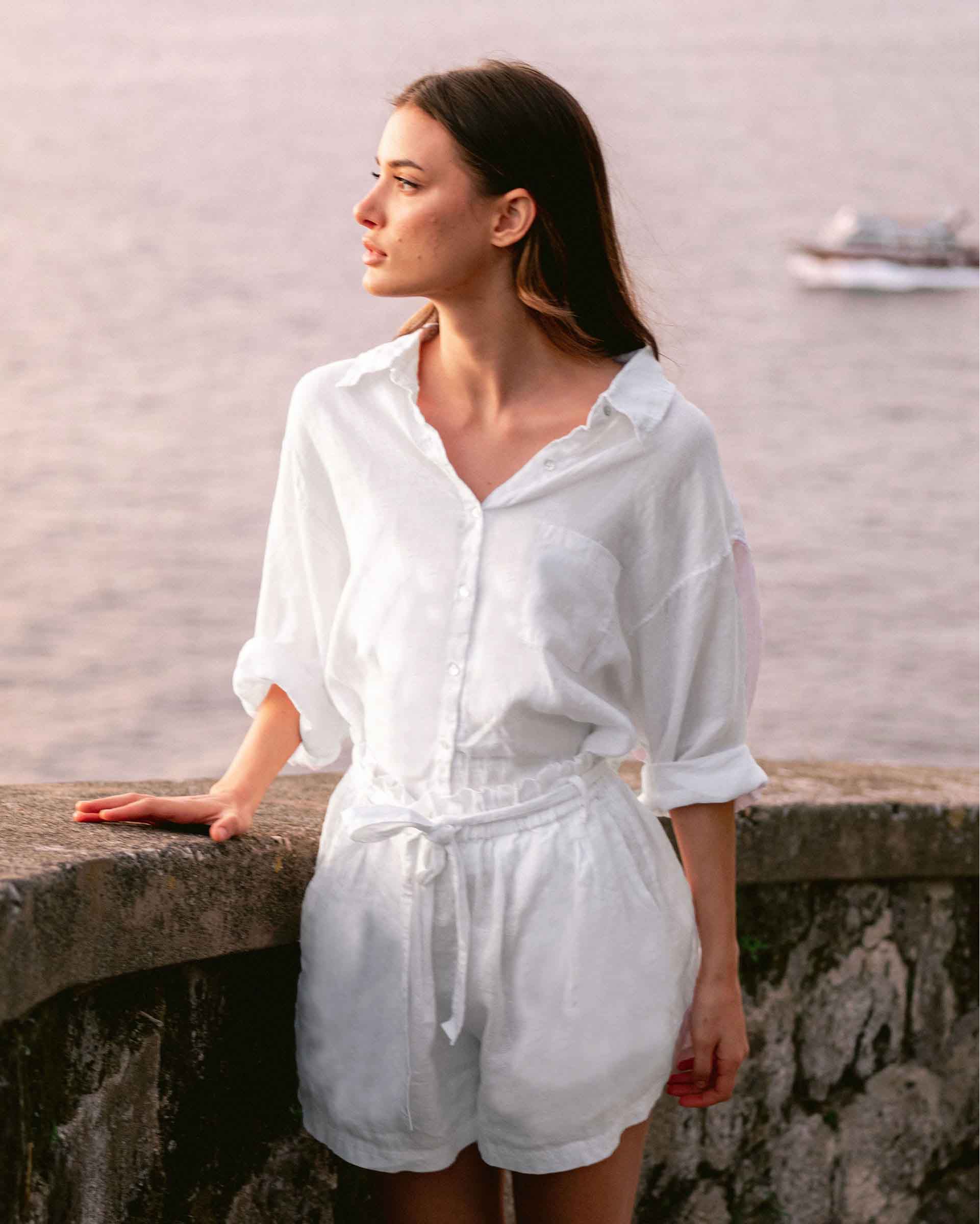 Female wearing a white button shirt and matching short in front of the ocean at sunset