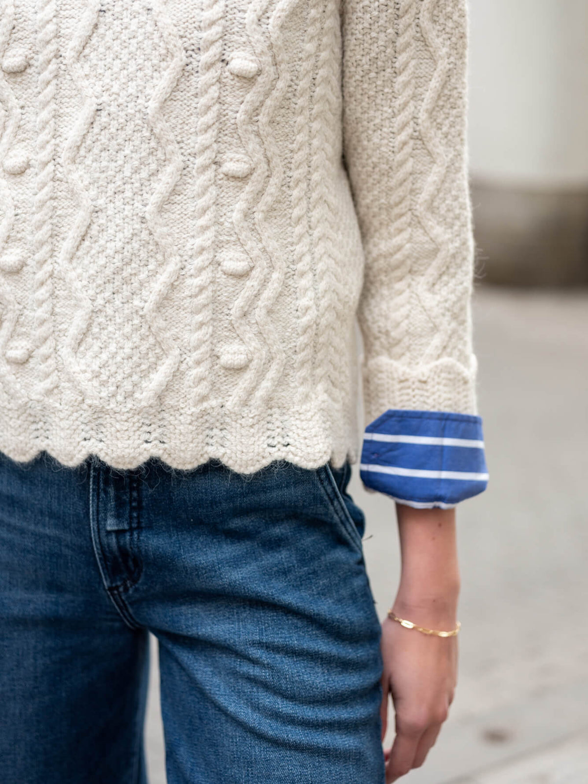 Cream cable-knit sweater with blue and white striped cuffs