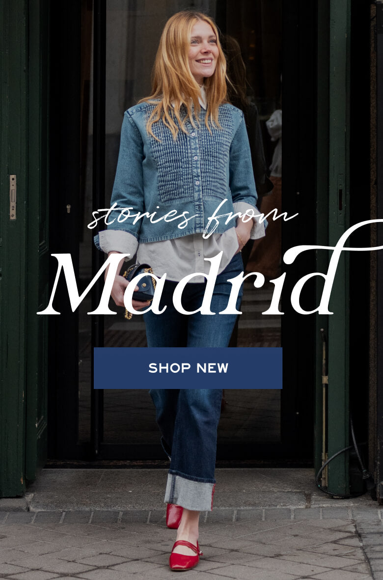 A woman in a blue knit cardigan and cuffed jeans standing in a doorway. Text: 'stories from Madrid' and 'SHOP NEW'.
