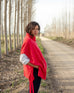 profile of woman wearing mersea cape poncho sweater in hibiscus red standing near a road