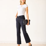 Woman wearing a white t-shirt and black jeans holding a black clutch against a white background