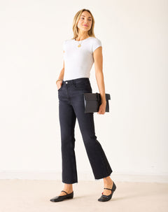 Woman wearing a white t-shirt and black jeans holding a black clutch against a white background