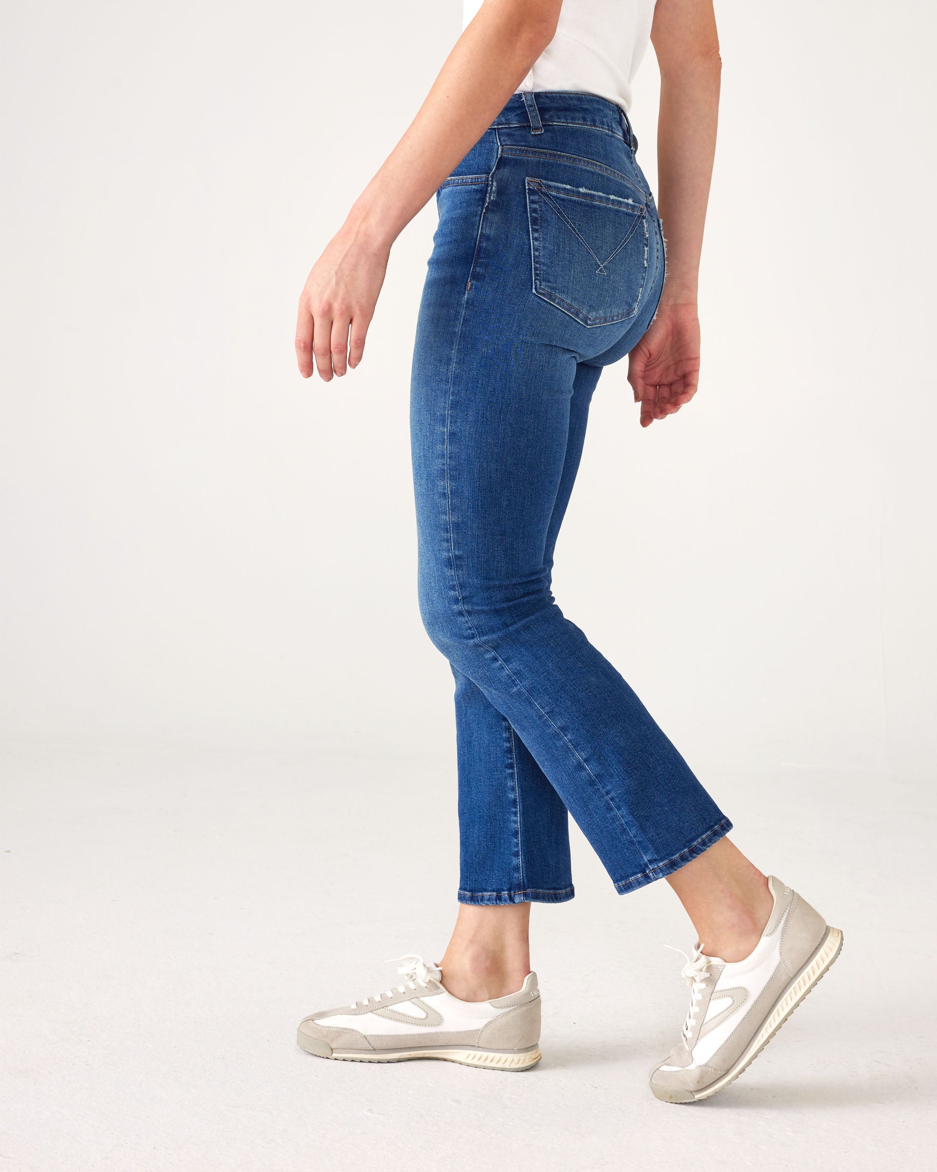 lower body side view of Woman wearing Mersea Infinity blue Nomad cropped mini boot-cut jeans standing on white background