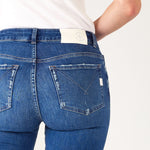 Closeup rear view of Woman wearing Mersea Infinity blue Nomad cropped mini boot-cut jeans standing against white background