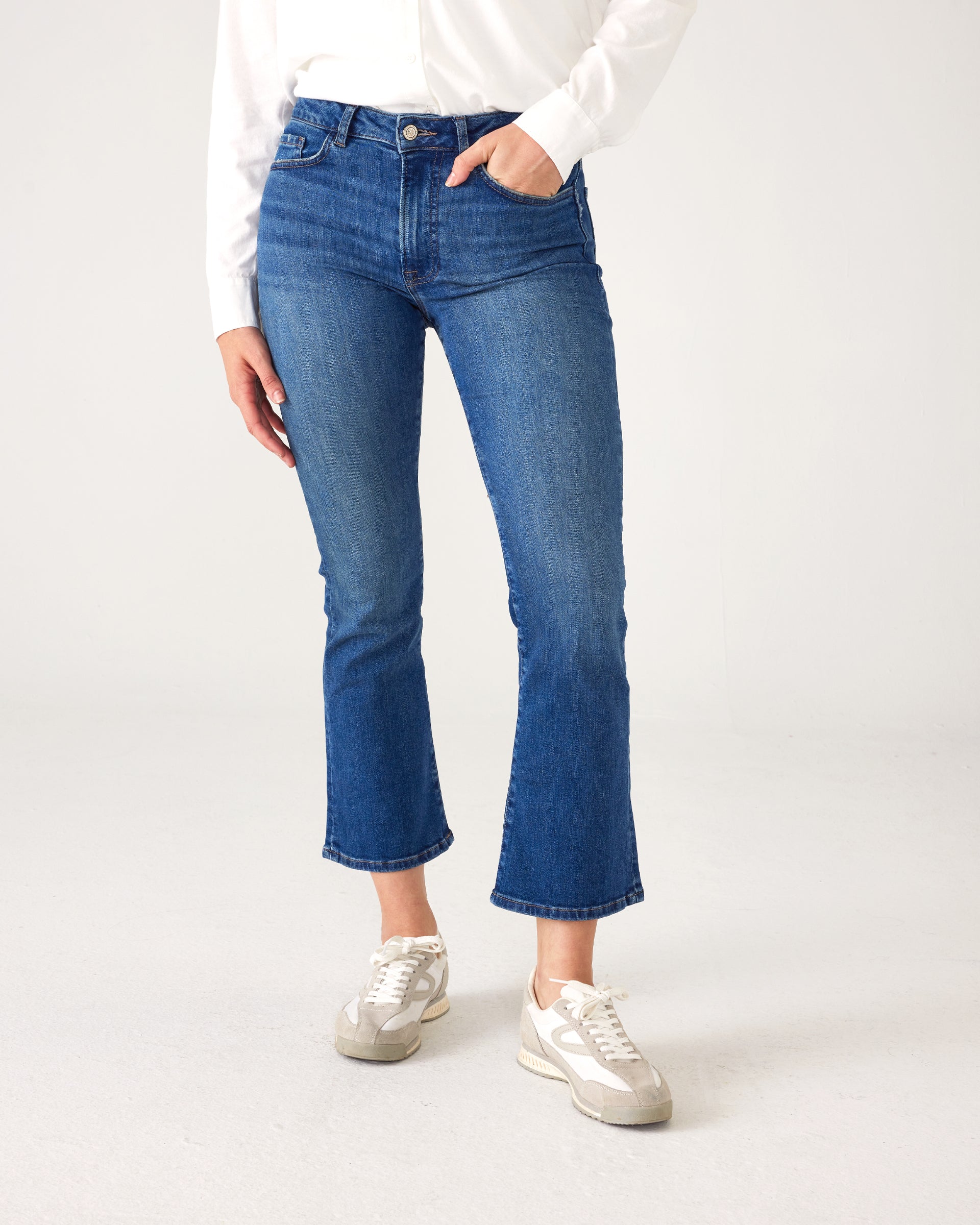 lower body of Woman wearing Mersea Infinity blue Nomad cropped mini boot-cut jeans standing against white background